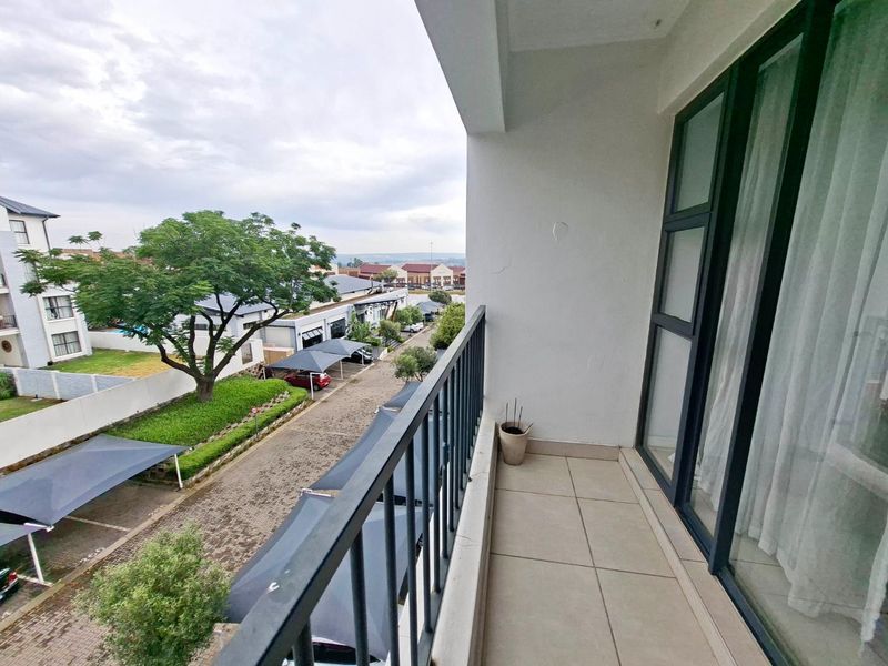 A clean, tiled balcony featuring a metal balustrade and sliding glass door access, offering an elevated view of the complex grounds.