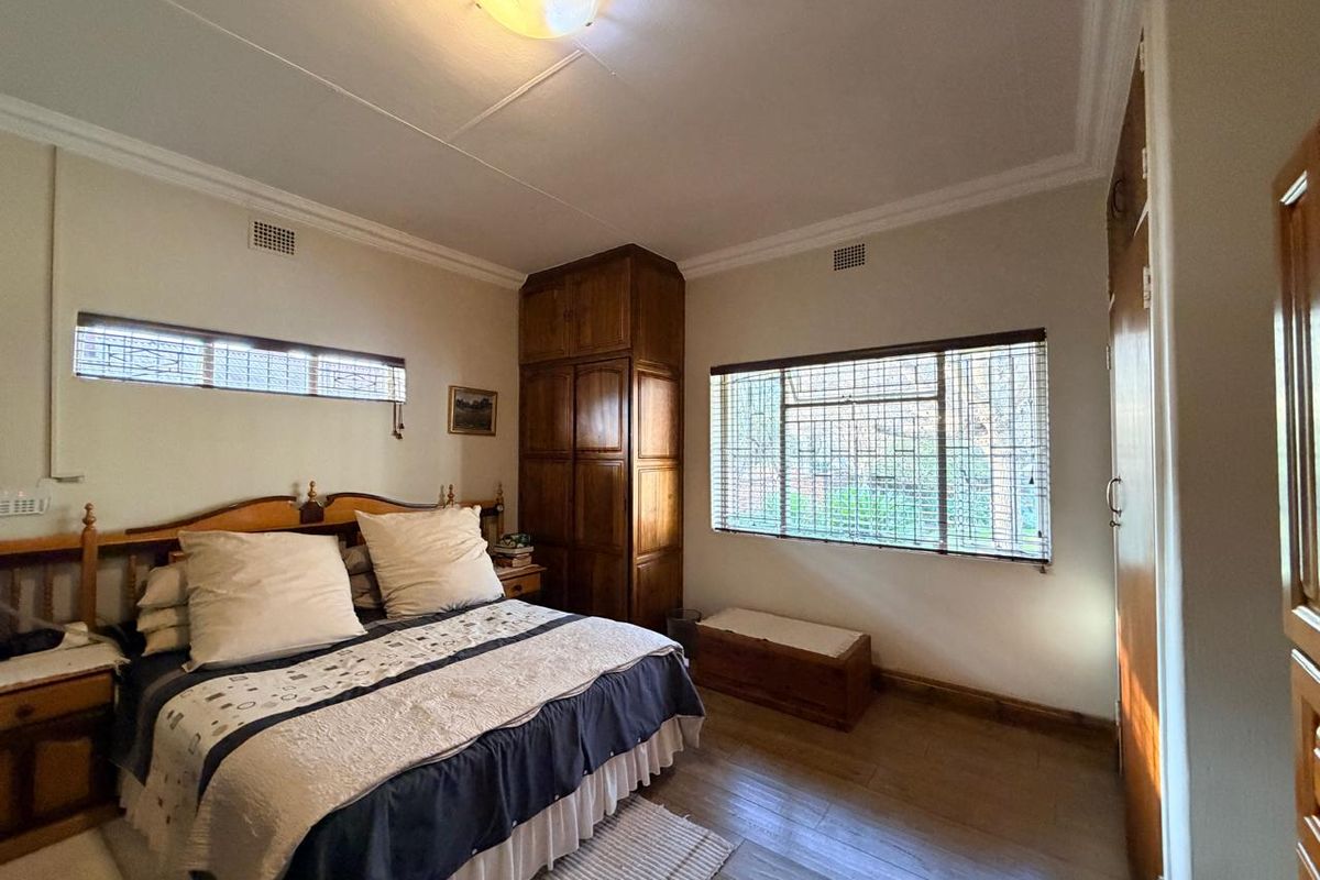 A bedroom featuring built-in wooden cupboards, laminate flooring, and security bars on the windows, offering a functional space with classic finishes.