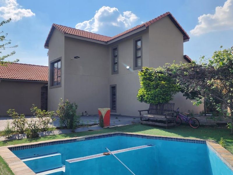 Rear view of the townhouse featuring a swimming pool, paved patio area, and a two-story exterior facade with a tiled roof.