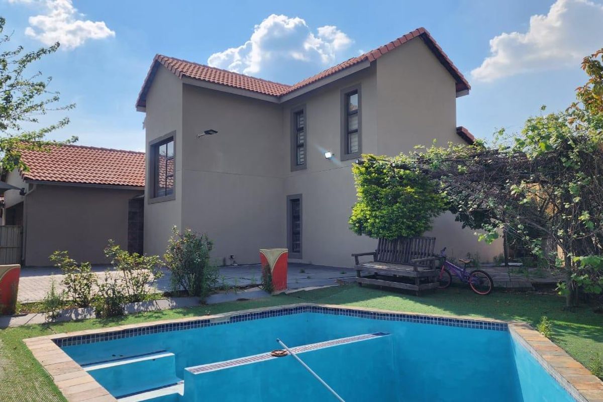 Rear view of the townhouse featuring a swimming pool, paved patio area, and a two-story exterior facade with a tiled roof.