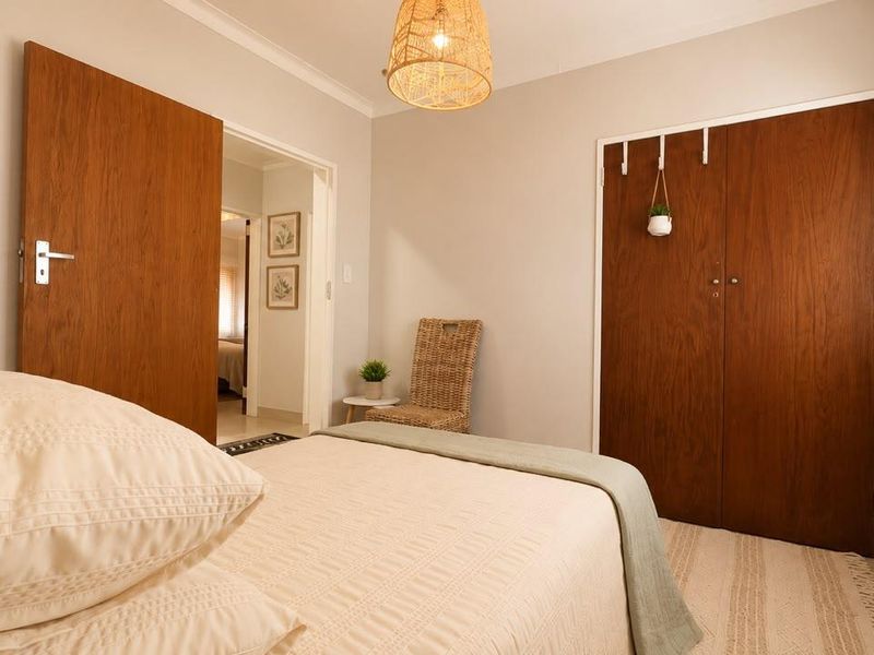 A well-maintained bedroom featuring built-in wooden cupboards, neutral wall finishes, and natural light through venetian blinds.