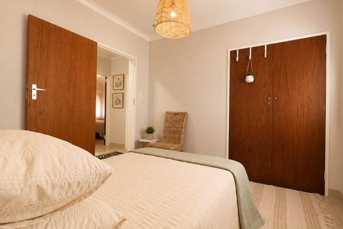A well-maintained bedroom featuring built-in wooden cupboards, neutral wall finishes, and natural light through venetian blinds.