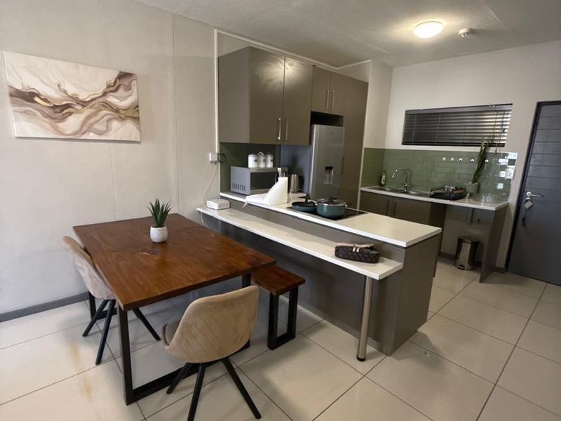 Modern open-plan kitchen and dining area featuring sleek cabinetry, stone countertops, tiled flooring, and a functional breakfast bar layout.