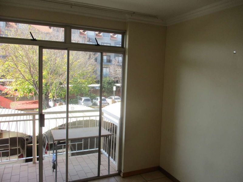 An empty living area featuring tiled flooring, cornice detailing, and a sliding glass door providing access to a private balcony.