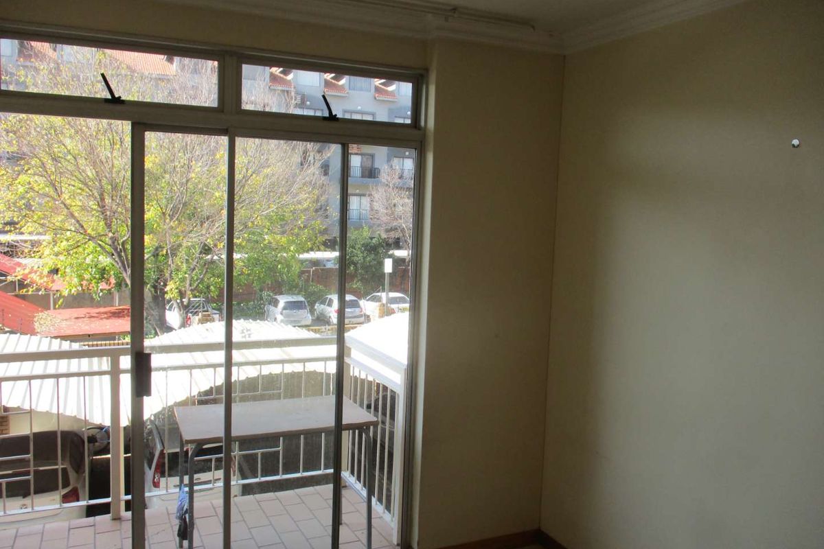 An empty living area featuring tiled flooring, cornice detailing, and a sliding glass door providing access to a private balcony.