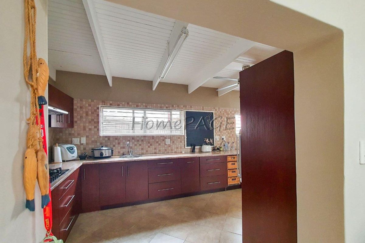 A functional kitchen featuring dark wood cabinetry, tiled backsplash, and a white exposed beam ceiling, offering a practical layout for daily meal preparation.