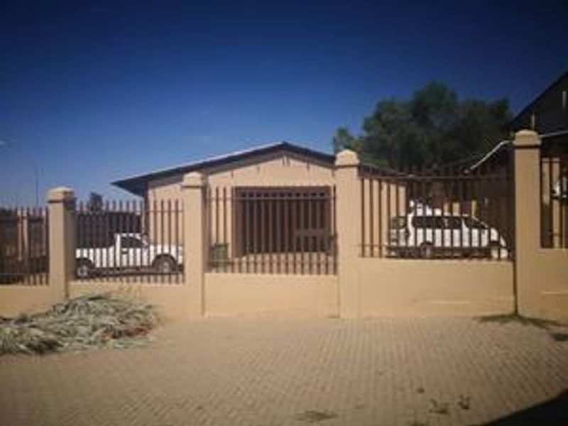 Front exterior view of the industrial property featuring a secure perimeter wall with steel palisade fencing and a paved driveway leading to the garage.