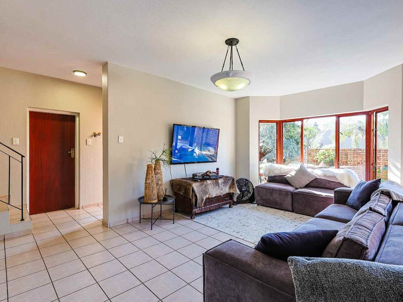 Spacious living room featuring tiled flooring, a large bay window providing natural light, and an adjacent staircase with a metal railing.