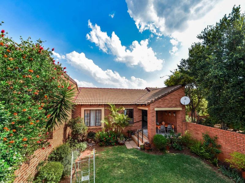A rear view of the townhouse featuring a private garden, brick facade, and a covered patio area perfect for outdoor relaxation.