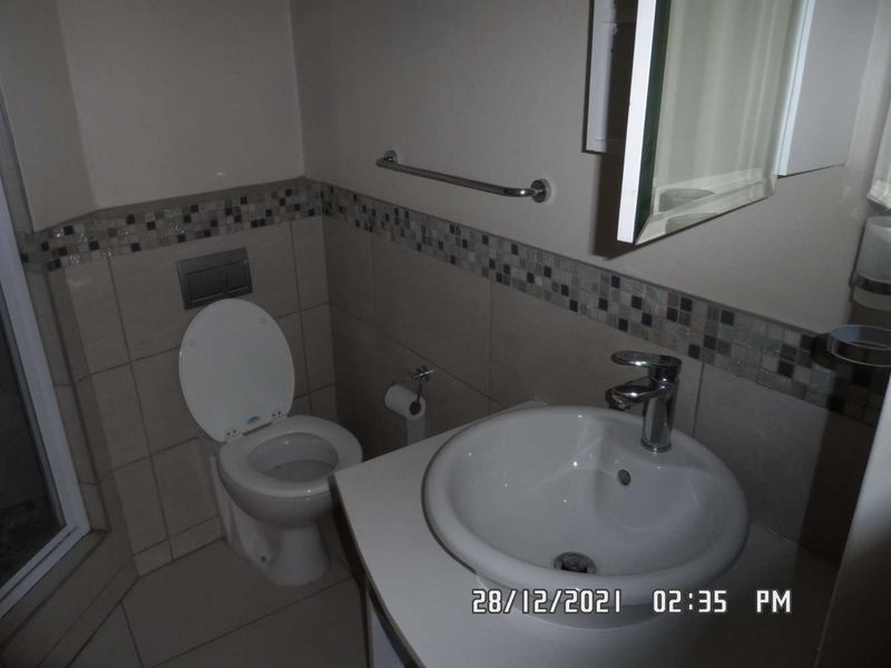 A compact bathroom featuring a wall-mounted toilet, vanity basin with chrome mixer tap, and a decorative mosaic tile border.