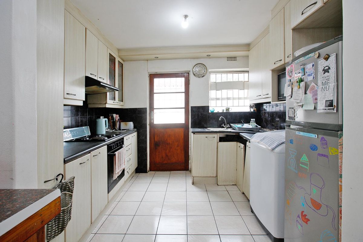 A functional kitchen featuring light-toned cabinetry, dark tiled splashbacks, a built-in oven and hob, and direct access to the exterior.