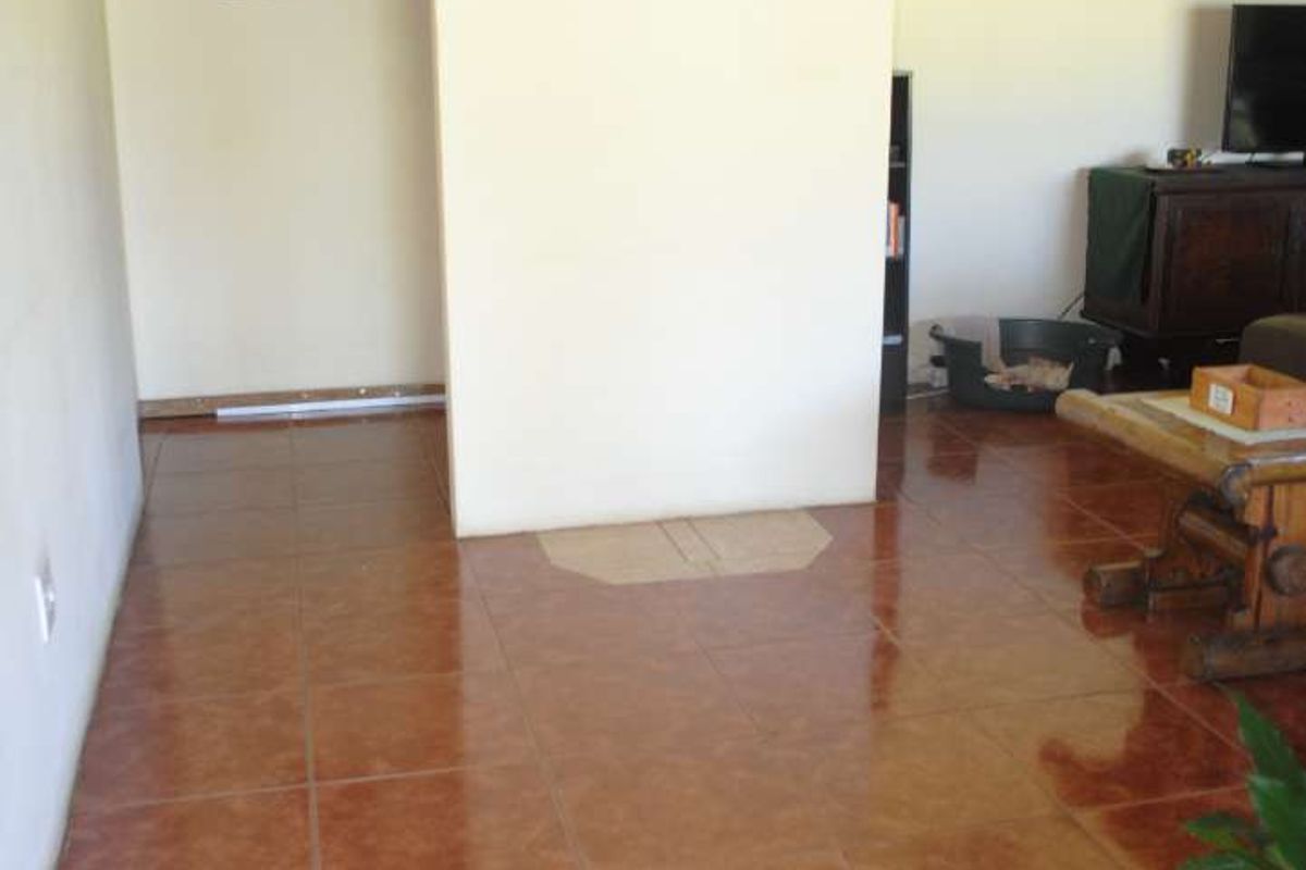 A living area featuring terracotta-style floor tiles and a central partition wall leading to an adjacent room.