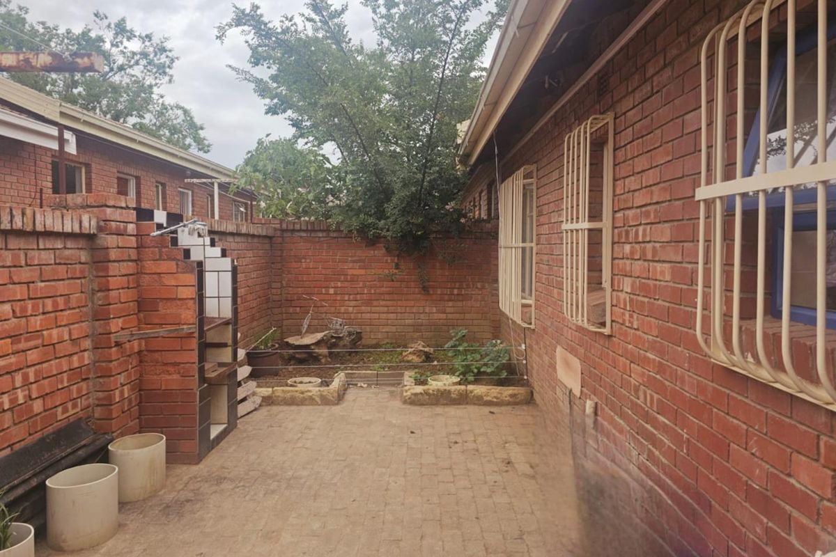 A private rear courtyard featuring exposed brick walls, paved flooring, and a built-in brick braai area with security bars on the windows.