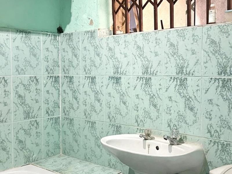 A dated bathroom featuring a pedestal basin, built-in bathtub, and tiled walls, requiring cosmetic updates and repairs to the wall finishes.