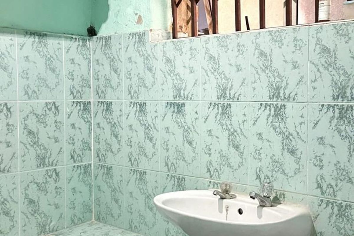 A dated bathroom featuring a pedestal basin, built-in bathtub, and tiled walls, requiring cosmetic updates and repairs to the wall finishes.