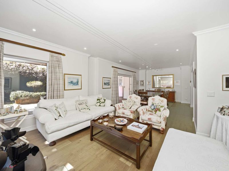 Spacious open-plan living and dining area featuring hardwood flooring, recessed lighting, and large windows providing natural light and garden views.