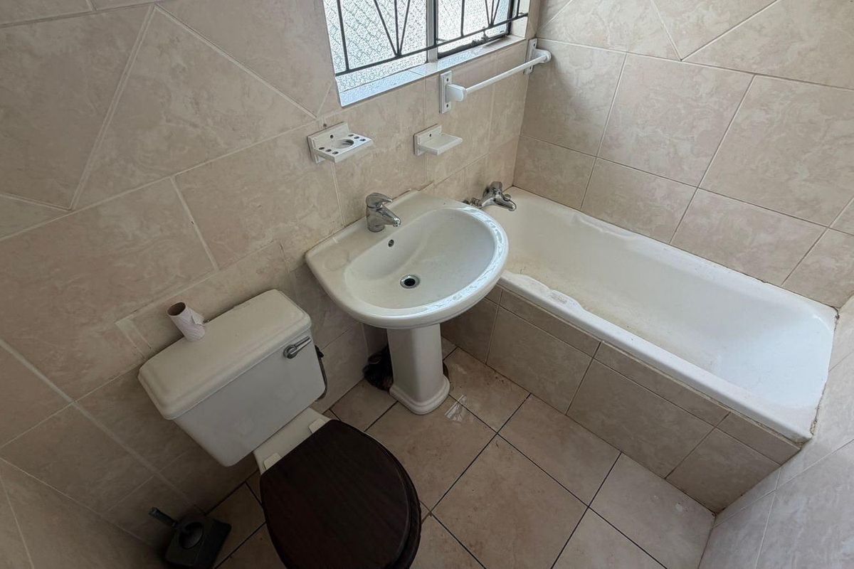 A compact bathroom featuring a pedestal basin, bathtub, and toilet with neutral ceramic wall and floor tiling.