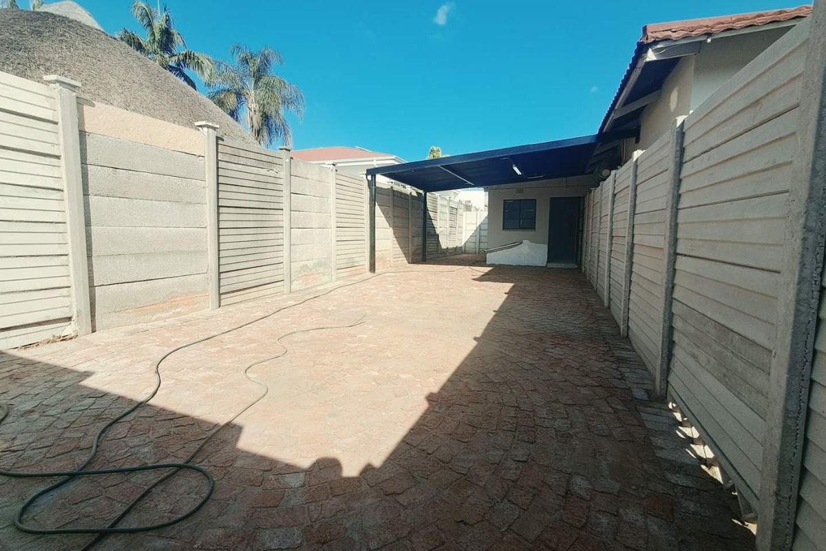 A spacious rear exterior area featuring paved flooring, enclosed by precast concrete walls, and including a covered carport structure.