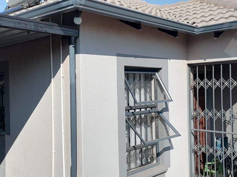 Rear exterior view of the house featuring a tiled roof, metal security gates on windows and doors, and a covered carport area.