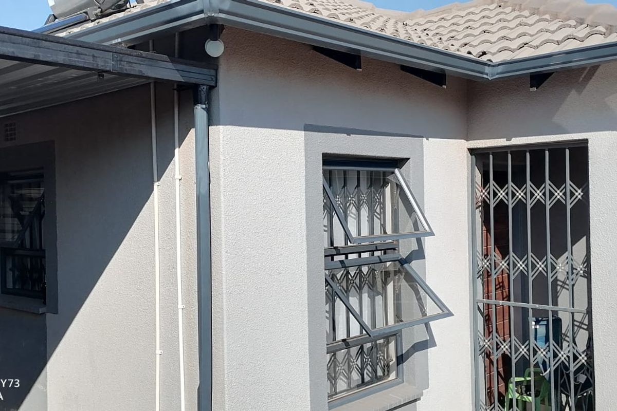 Rear exterior view of the house featuring a tiled roof, metal security gates on windows and doors, and a covered carport area.