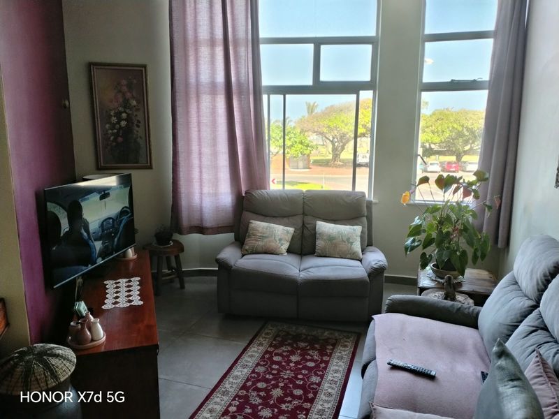 A living room featuring large windows that provide natural light and views of the surrounding area, complemented by tiled flooring.