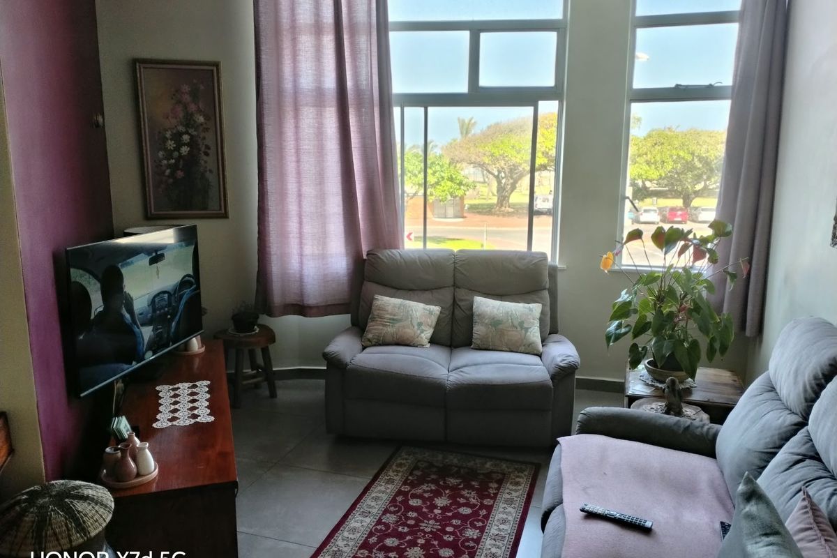 A living room featuring large windows that provide natural light and views of the surrounding area, complemented by tiled flooring.