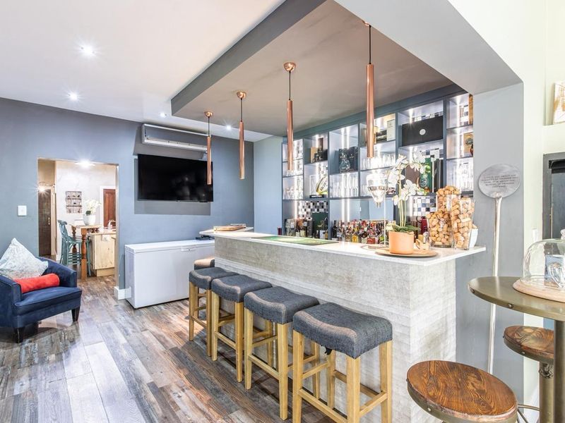 A well-appointed home bar area featuring a built-in counter, integrated shelving, modern pendant lighting, and durable laminate flooring.