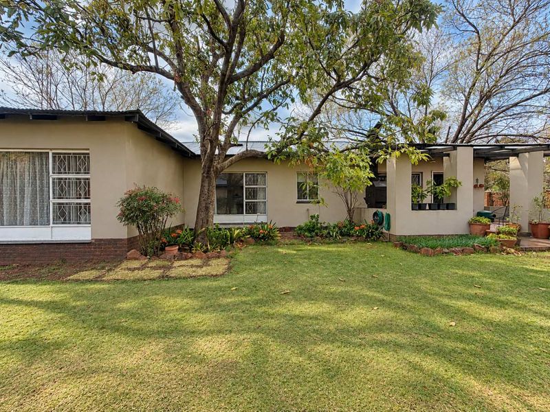 Rear view of the house featuring a lawn, mature trees, and a covered patio area with security bars on the windows.