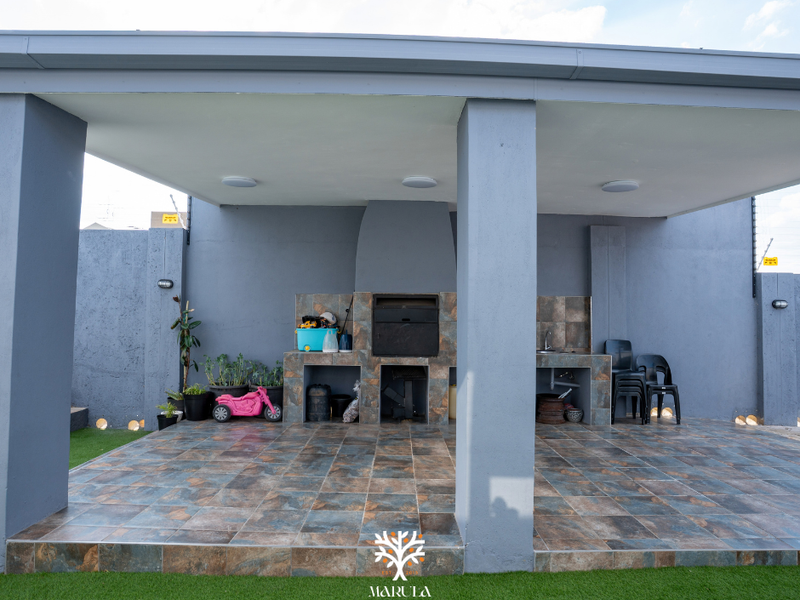 A covered outdoor patio featuring a built-in braai, tiled flooring, and a sink, providing a functional space for outdoor entertaining.