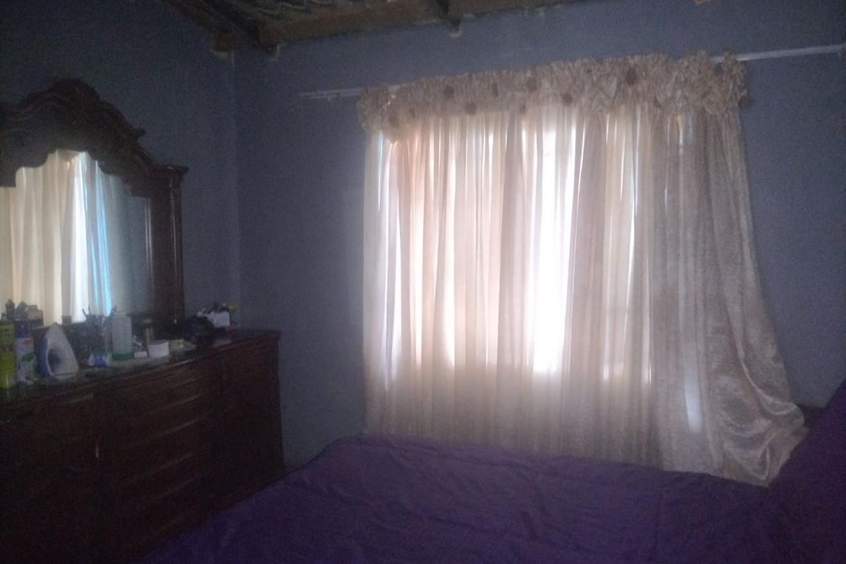 A bedroom featuring exposed ceiling rafters and a window with curtains, providing a basic sleeping space.
