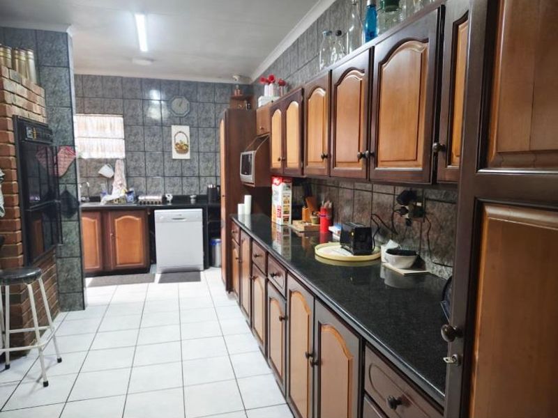 A functional kitchen featuring dark wood cabinetry, granite countertops, a double wall oven, and full-height wall tiling.