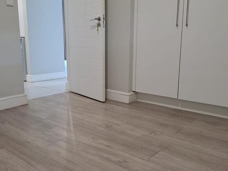 A clean, empty bedroom featuring modern light-toned laminate flooring and built-in cupboards with a neutral interior finish.