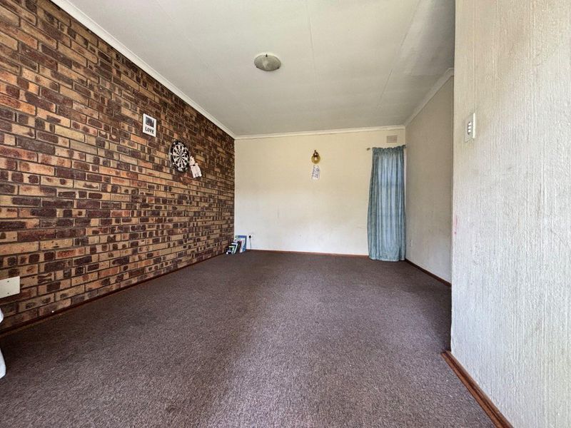 A spacious living room featuring an exposed brick feature wall, neutral painted walls, and carpeted flooring, offering a blank canvas for interior design.