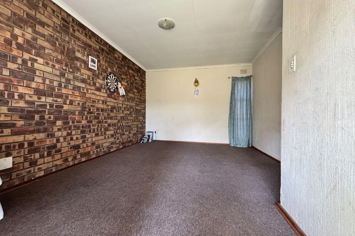 A spacious living room featuring an exposed brick feature wall, neutral painted walls, and carpeted flooring, offering a blank canvas for interior design.