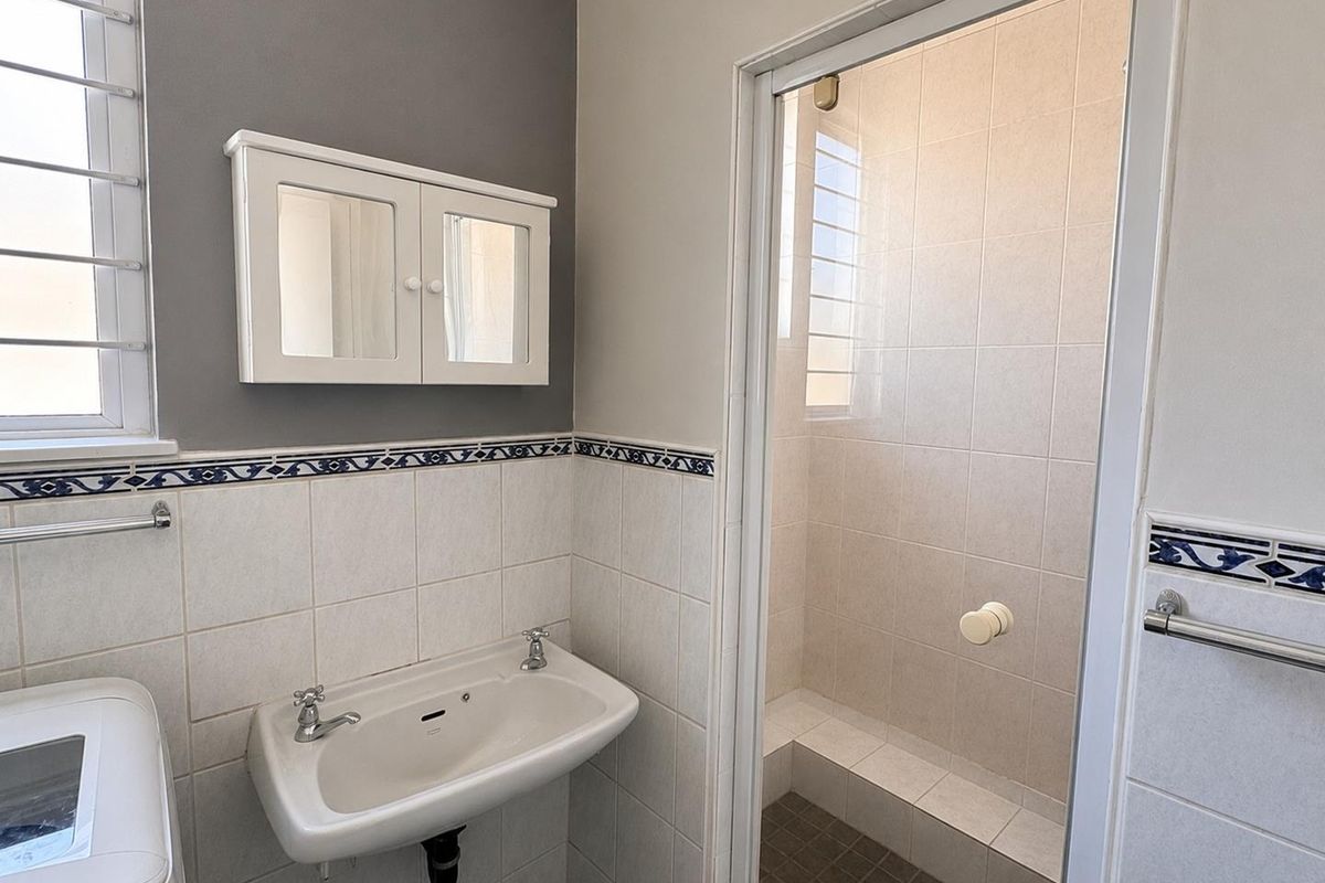 A functional bathroom featuring a wall-mounted basin, a tiled shower enclosure, and a wall-mounted medicine cabinet with neutral wall finishes.