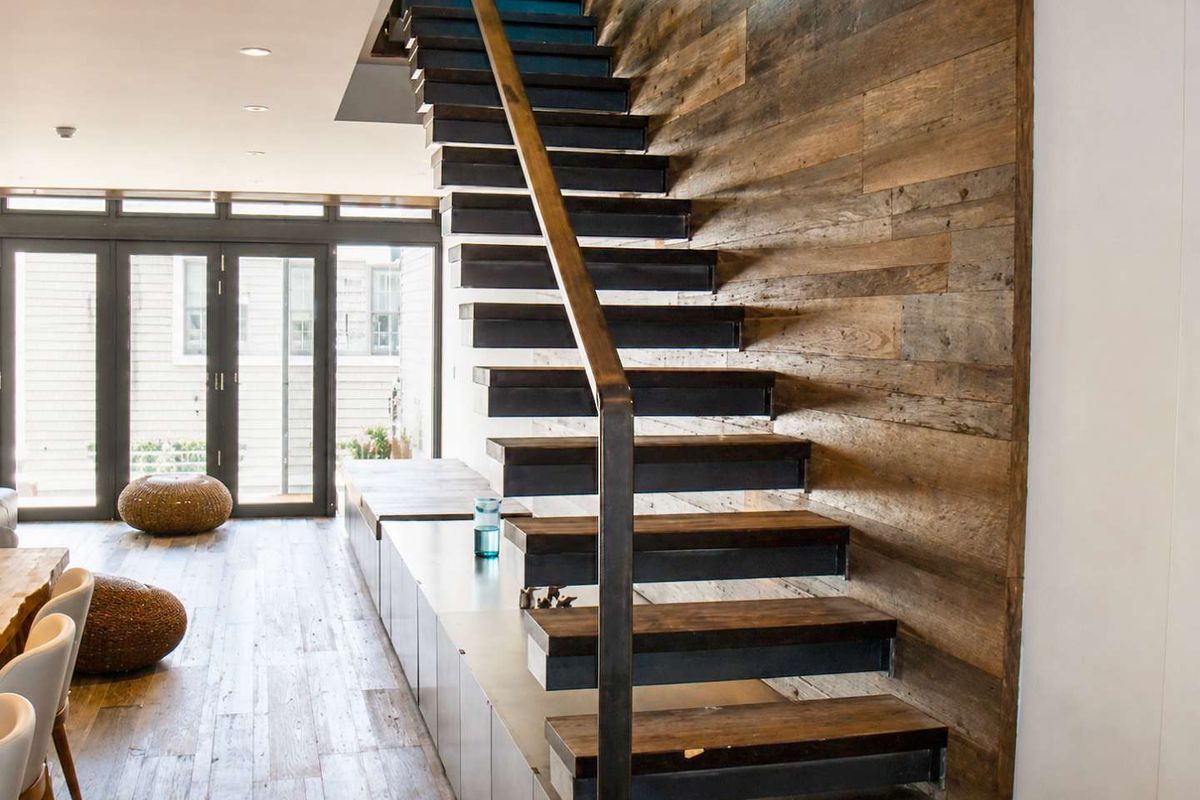 Modern living area featuring a striking open-tread staircase with timber wall cladding, built-in storage cabinetry, and seamless access to the outdoors via bi-fold doors.