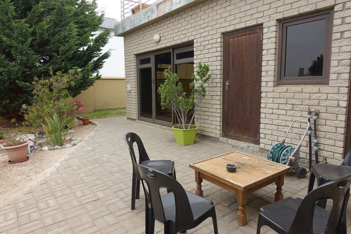 A paved rear patio area featuring brick exterior walls, sliding glass doors, and a wooden door, providing direct access to the garden space.