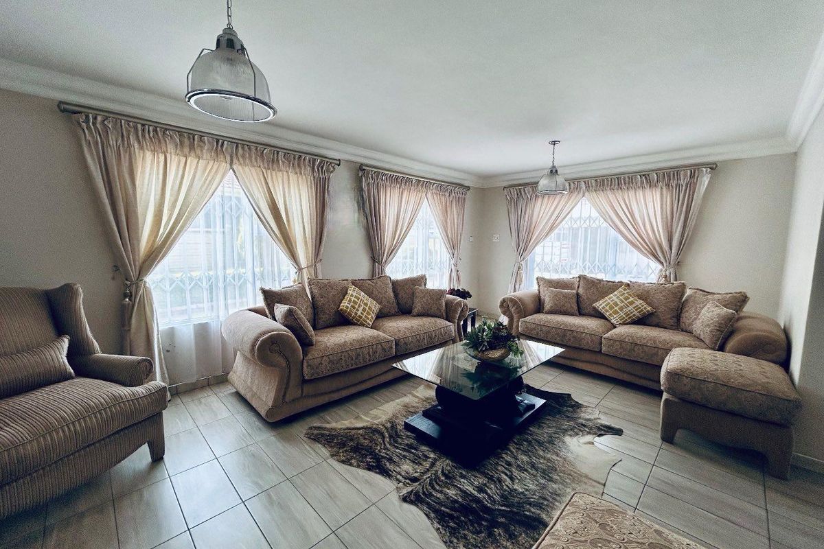 A spacious living room featuring neutral tiled flooring, large windows with curtain treatments, and modern pendant lighting.