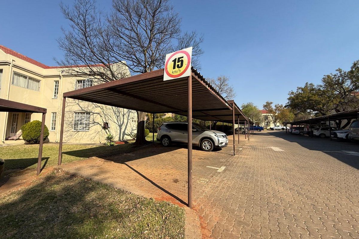 Outdoor parking area featuring covered carports with paved surfacing, situated adjacent to the apartment building complex.