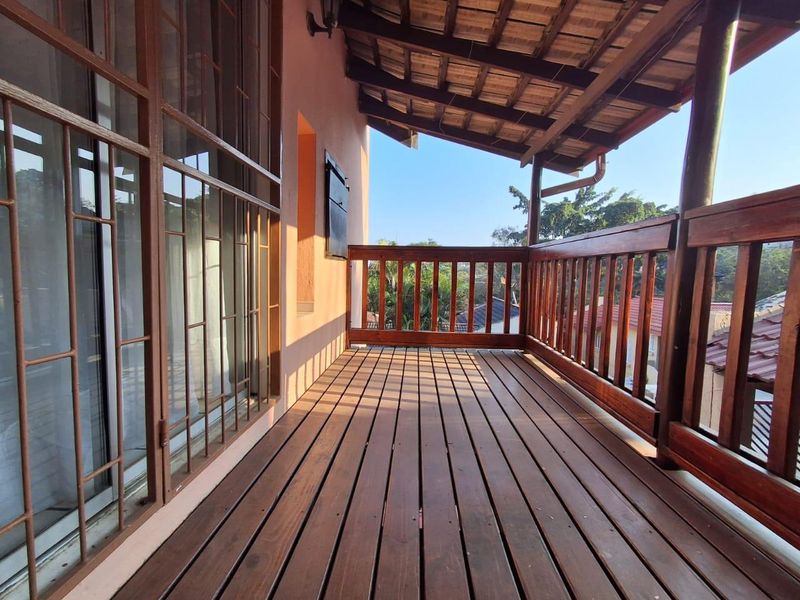 A covered timber balcony featuring wooden decking, a matching balustrade, and exposed roof rafters, offering an elevated outdoor space.