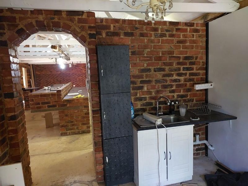 A rustic kitchen area featuring exposed brick walls, an arched entryway, and basic cabinetry, currently in an unfinished state requiring renovation.