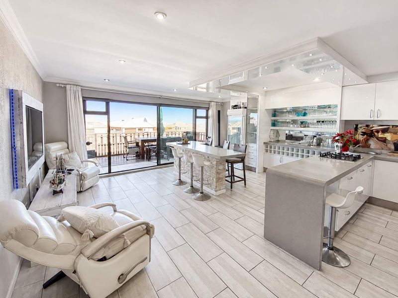 Spacious open-plan living and kitchen area featuring a stone-clad island, modern cabinetry, and large sliding doors leading to an outdoor deck.
