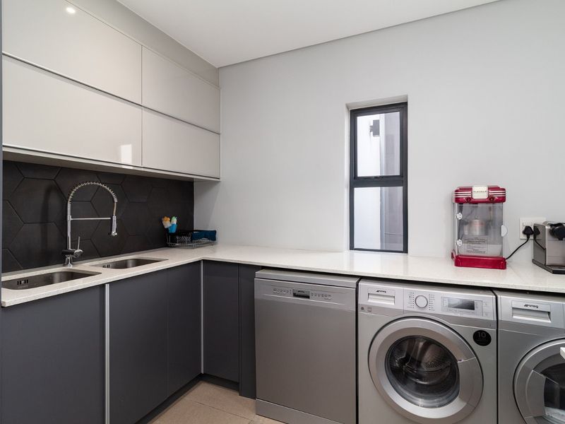 Modern laundry room featuring sleek grey cabinetry, stone countertops, a double sink with gooseneck tap, and integrated laundry appliances.