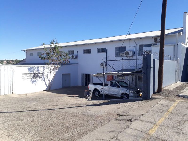 Front exterior view of an industrial property featuring a concrete driveway, security fencing, and multiple external air conditioning units.