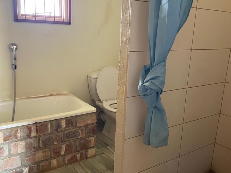 A functional bathroom featuring a brick-surround bathtub, a separate shower enclosure, and a toilet, with tiled flooring and wall finishes throughout.