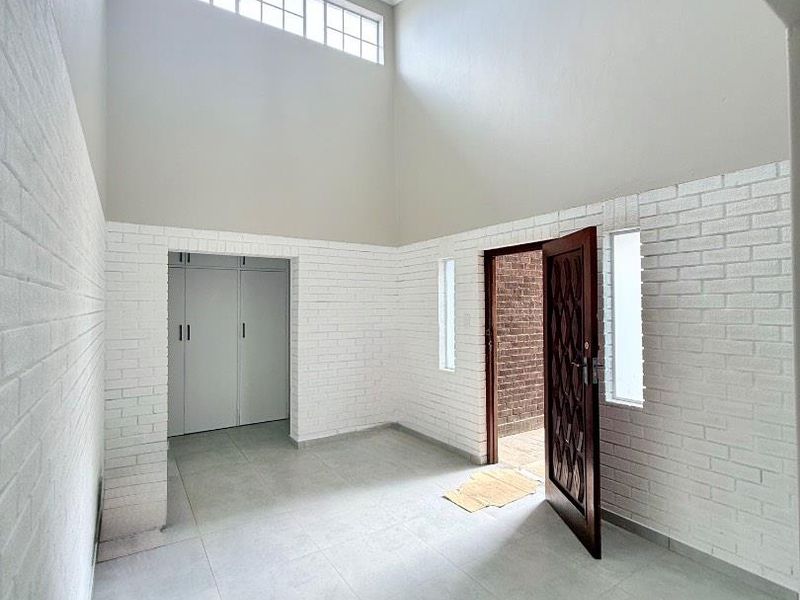 Spacious double-volume entrance hall featuring white-painted exposed brick walls, large clerestory windows, modern pendant lighting, and neutral tiled flooring.