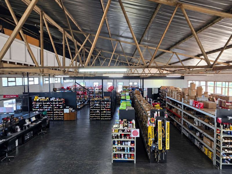 Spacious industrial warehouse featuring high exposed steel roof trusses, mezzanine level, and extensive fixed steel shelving units for storage and retail display.