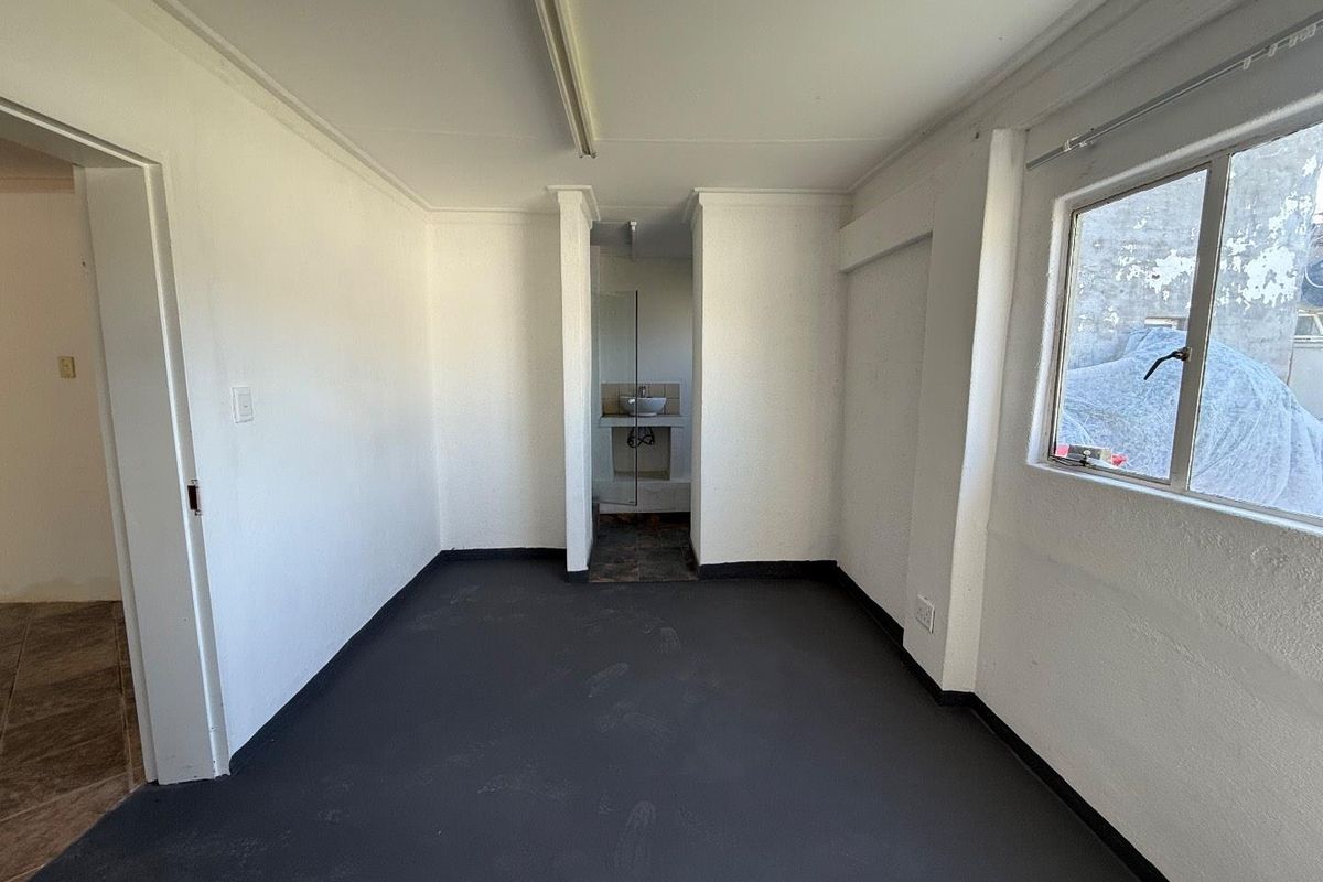 An empty bedroom featuring a simple layout with an attached small basin area and neutral finishes, ready for renovation or staging.
