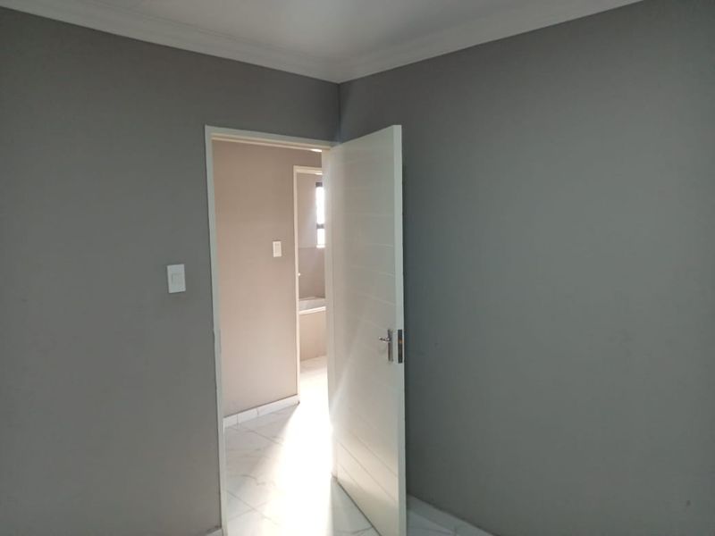 A clean, empty bedroom featuring neutral grey walls, white tiled flooring, and a modern internal door leading to an adjacent bathroom area.
