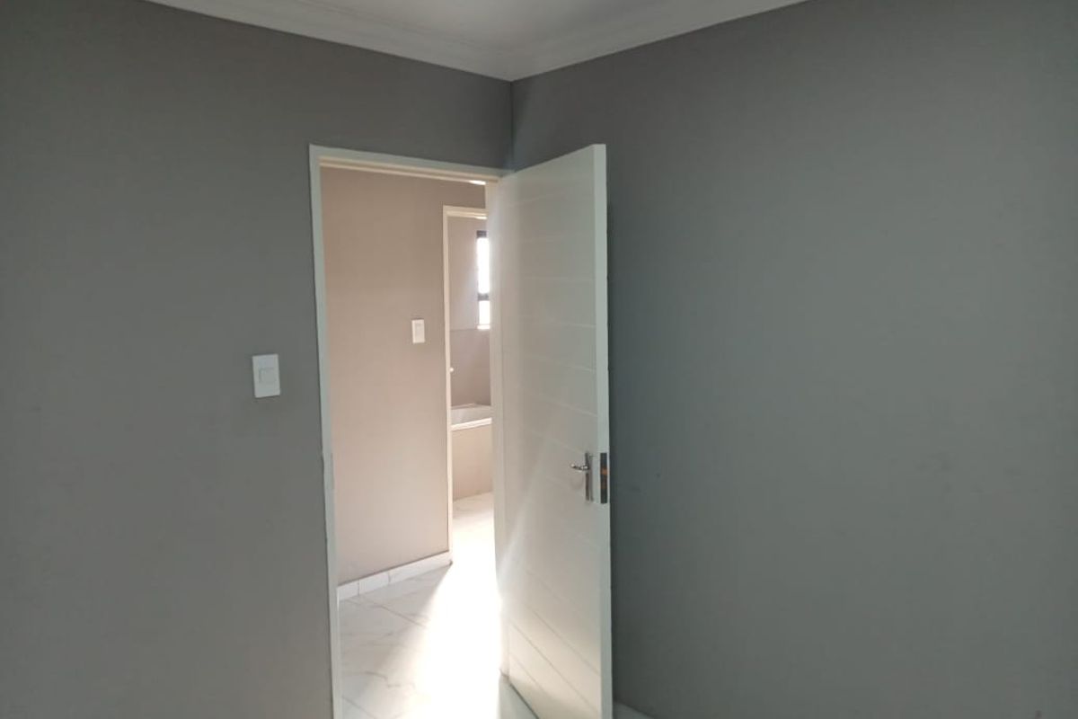 A clean, empty bedroom featuring neutral grey walls, white tiled flooring, and a modern internal door leading to an adjacent bathroom area.